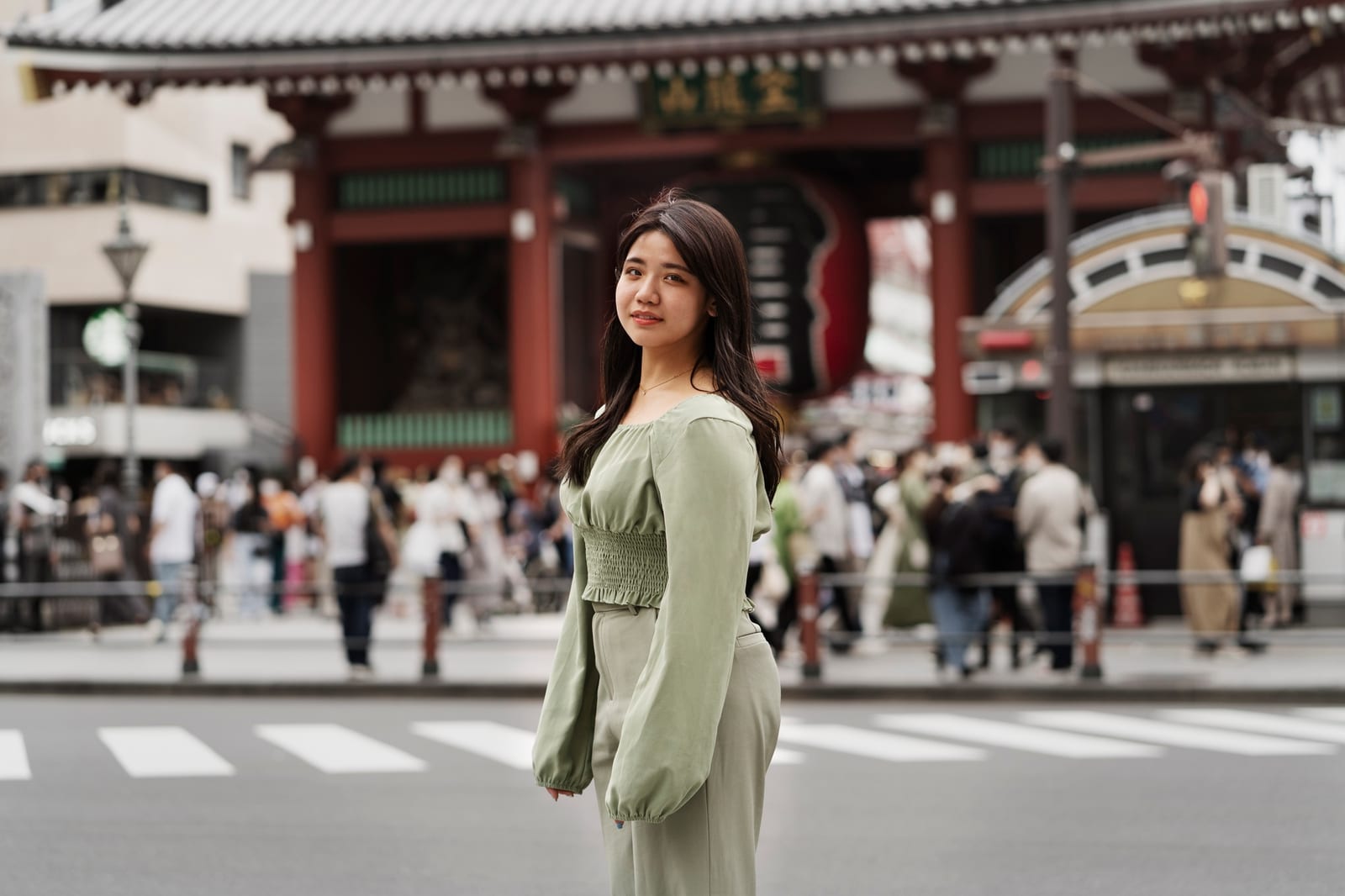 緑色の装いの女性が鳥居の前の横断歩道に立っている様子。